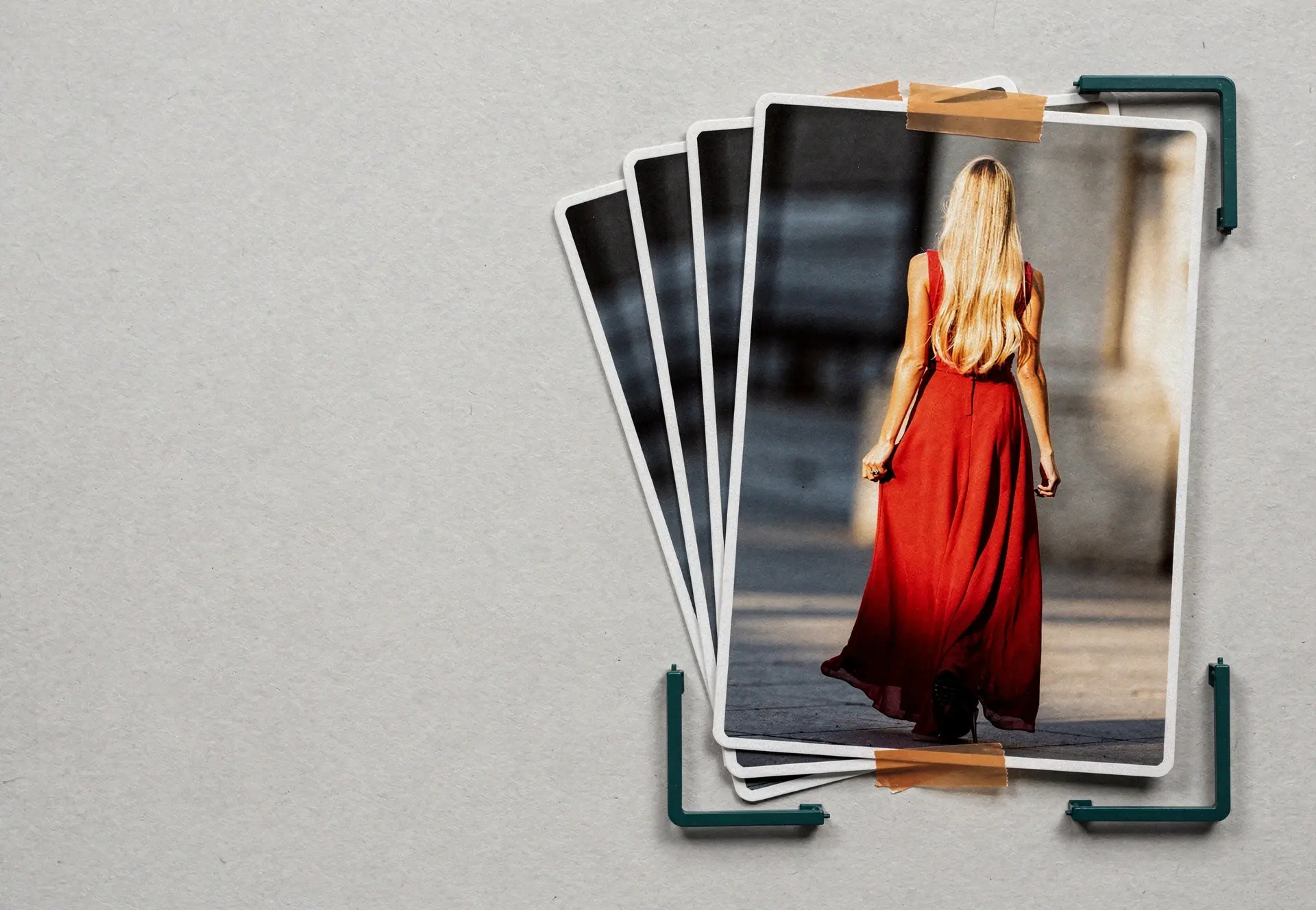 A fanned deck of photographic prints on porcelain paper, the top one a full-length photograph of a tall blonde woman in a long red dress walking away from the camera, framed by petrol corner registration brackets like a photo on a scan bed.